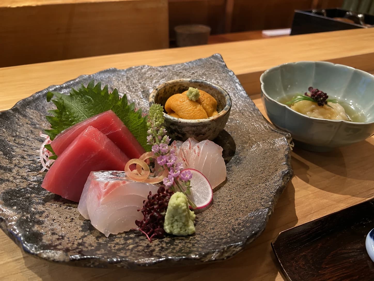AI-generated sample guest photo: seasonal sashimi and sea urchin on handmade ceramics at a Japanese counter